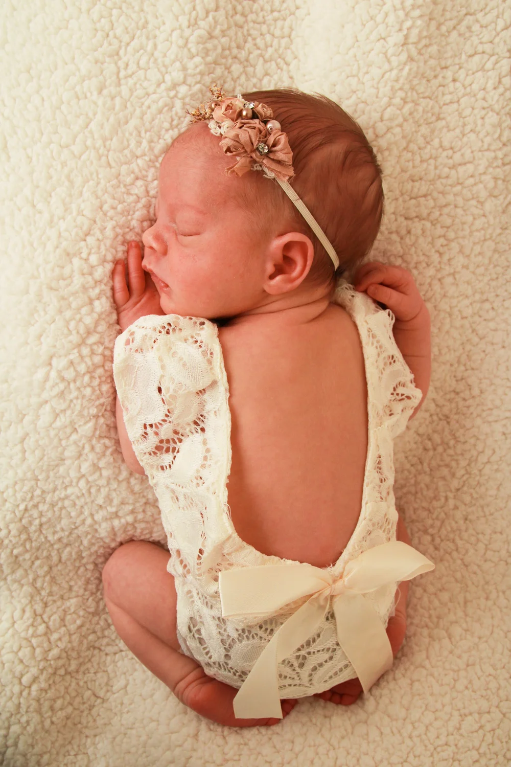 Back view of a newborn baby girl wearing a lace romper with a bow, styled for a Long Island newborn photography session
