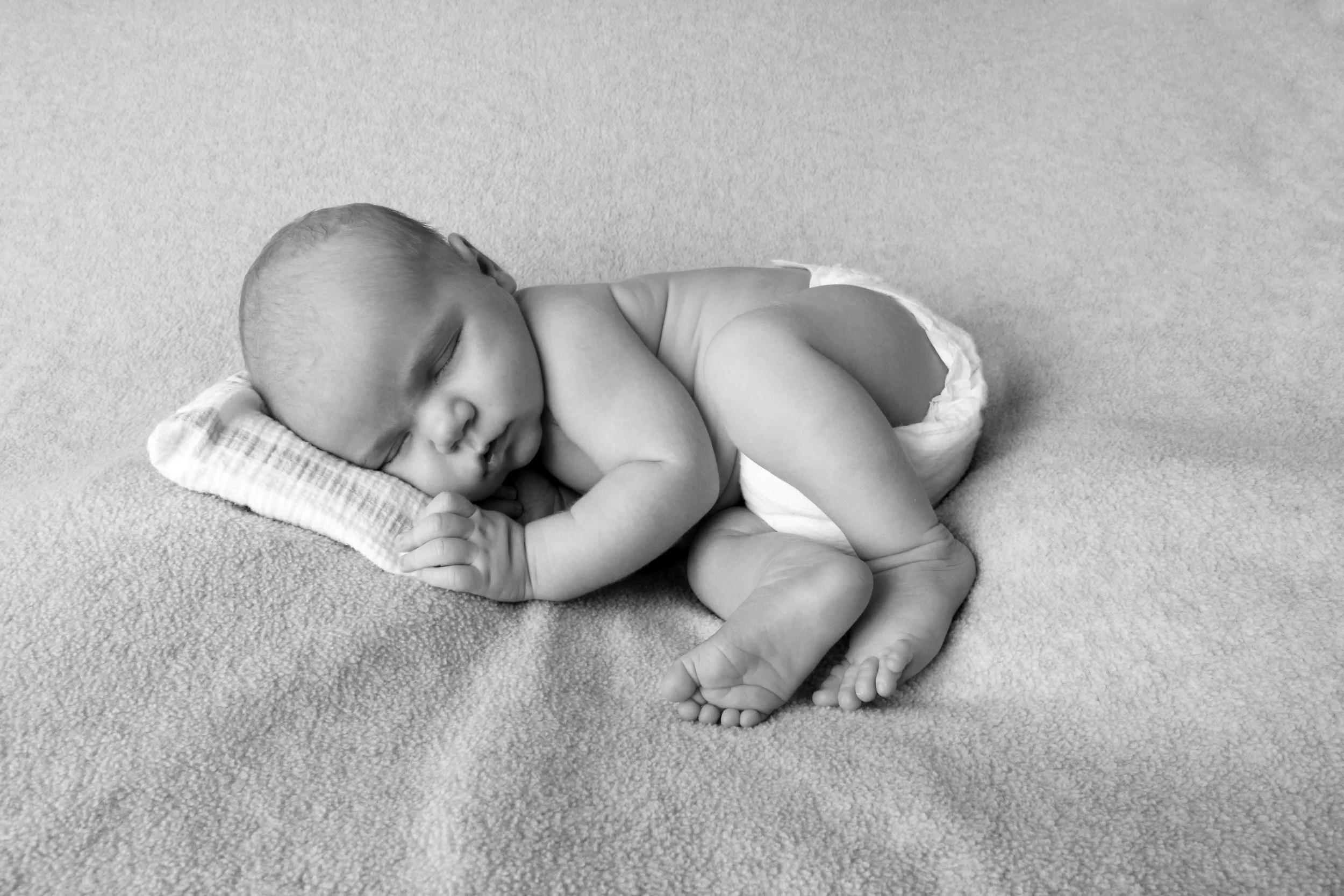 Black and white portrait of a sleeping newborn baby curled up on a soft blanket, captured during a Nassau County newborn session